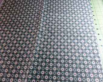 May include: A close-up of a teal fabric with a repeating pattern of white circles and brown squares.