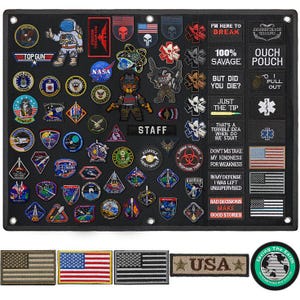 May include: A black rectangular display board featuring a large collection of embroidered patches, including various space, military, and humorous designs. The board includes rectangular text patches and several flag patches, with additional loose flag and circular patches below.