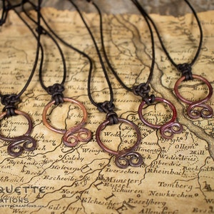 May include: Five copper wire necklaces with different designs, including a circle and a swirl, on a brown leather cord. The necklaces are displayed on a vintage map.