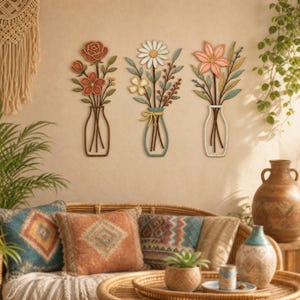 May include: Three wall-mounted metal art pieces depicting flowers in vases. The left piece shows a rose and small flowers in a brown vase. The center piece features a daisy and yellow flowers in a blue vase. The right piece displays a lily in a white vase.
