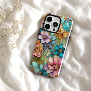 May include: A smartphone case featuring a vibrant, multi-coloured floral pattern with gold-toned outlines. The design includes layered petals in shades of teal, pink, orange, and purple, with a prominent triple-lens camera cutout at the top.