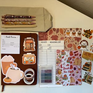 May include: A beige corduroy pencil case with four pens, a brown notebook with a book review insert, two reading list sheets, a small plastic container of sticky notes, two rolls of washi tape, and various autumn-themed stickers.
