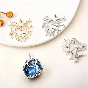 Può includere: Tre ciondoli in metallo a forma di strutture di corallo ramificate, uno color oro, uno color argento e uno color argento che racchiude una pietra preziosa sfaccettata blu intenso. Ogni pezzo è dotato di un occhiello per la catenina.