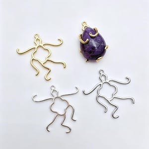 Peut inclure: Un pendentif en pierre violette en forme de goutte serti dans une monture en métal doré avec quatre griffes incurvées, accompagné de trois montures de pendentif vides en métal doré et argenté, chacune avec un trèfle central et quatre bras ondulés.