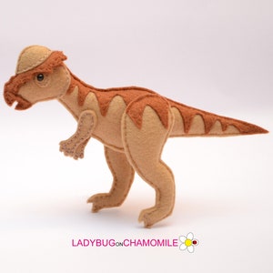 May include: A brown and tan felt Pachycephalosaurus dinosaur toy. The dinosaur has a distinctive dome-shaped head and a short, stout tail.