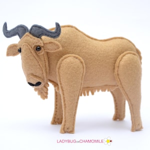 Puede incluir: Un animal de peluche de fieltro marrón con cuernos negros y puntas de cuernos grises. El animal tiene ojos negros y una boca cosida negra.