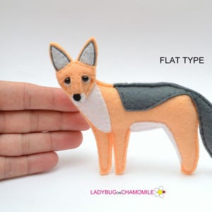 May include: A flat felt fox ornament in peach and dark gray with white chest detailing. The fox has black eyes and a black nose. The text FLAT TYPE is printed in the upper right corner, and LADYBUGONCHAMOMILE is printed at the bottom.