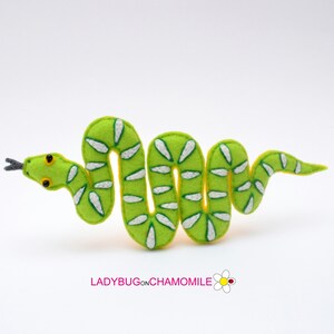 May include: A green felt snake with white markings, curled in a S shape. The snake has a yellow outline and black eyes.