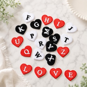 May include: A collection of heart-shaped embroidered patches in red, black, and white. Each patch features a single capital letter stitched in a contrasting color. The letters include F, G, H, I, J, K, L, M, O, P, Q, R, S, T, U, V, W, X, Z, and E.
