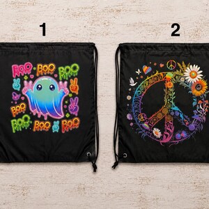 May include: Two black drawstring bags. Bag 1 features a colorful ghost with the text BOO and peace signs. Bag 2 displays a large peace sign symbol decorated with vibrant flowers, mushrooms, and small icons like hearts and butterflies.