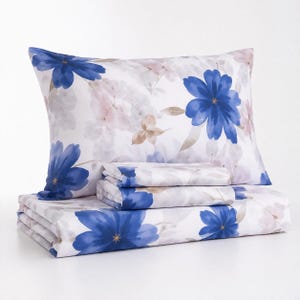 May include: A bedding set featuring a white background with a watercolor-style floral pattern in shades of vibrant blue and soft muted brown. The set includes a rectangular pillowcase and folded flat sheets, all displaying the same botanical print.