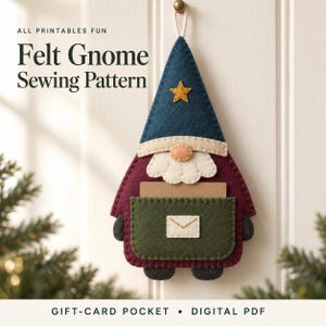 May include: A felt gnome ornament featuring a dark blue pointed hat with a yellow star, a cream-colored beard, a peach nose, and a maroon body. It includes a dark green pocket containing a brown card and a small white envelope with gold stitching.