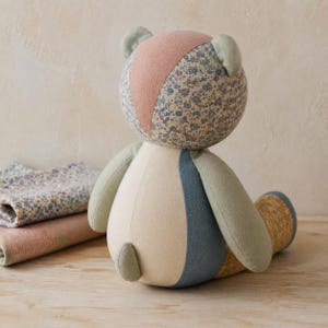 Op de afbeelding: Een knuffelbeer gemaakt van patchwork stoffen panelen in diverse kleuren en patronen, waaronder een bloemenprint, effen saliegroen, spijkerblauw, cr&egrave;me en mosterdgeel, voorzien van een klein staartje en ronde oren.
