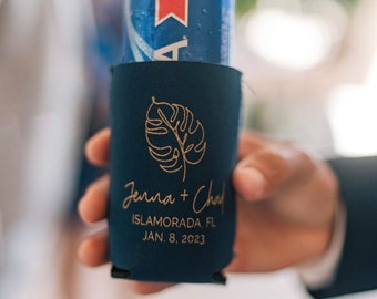 May include: A navy blue can cooler with a gold leaf design and the text "Jenna + Chad" "Islamorada, FL" "Jan. 8, 2023".