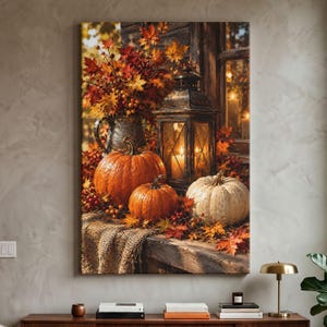 May include: A vertical wall art print depicting a rustic autumn scene with two orange pumpkins and one white pumpkin resting on a burlap-covered surface. A dark metal lantern with a glowing candle sits beside a pitcher filled with fall foliage.