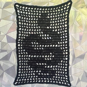 May include: A rectangular black crochet hammock featuring a grid-like open weave pattern. The piece is constructed with thin black yarn, creating a consistent square mesh design throughout the entire structure, suspended by four clear suction cups.