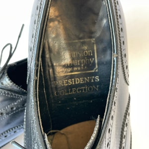 Puede incluir: Zapatos de vestir de cuero negro con dise&ntilde;o de punta de ala y cierre de cordones. Los zapatos tienen una etiqueta que dice "Johnston & Murphy Presidents Collection Made in U.S.A."