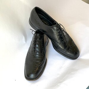 Puede incluir: Un par de zapatos Oxford de cuero negro con detalles de punta de ala. Los zapatos tienen cordones y est&aacute;n en buen estado.