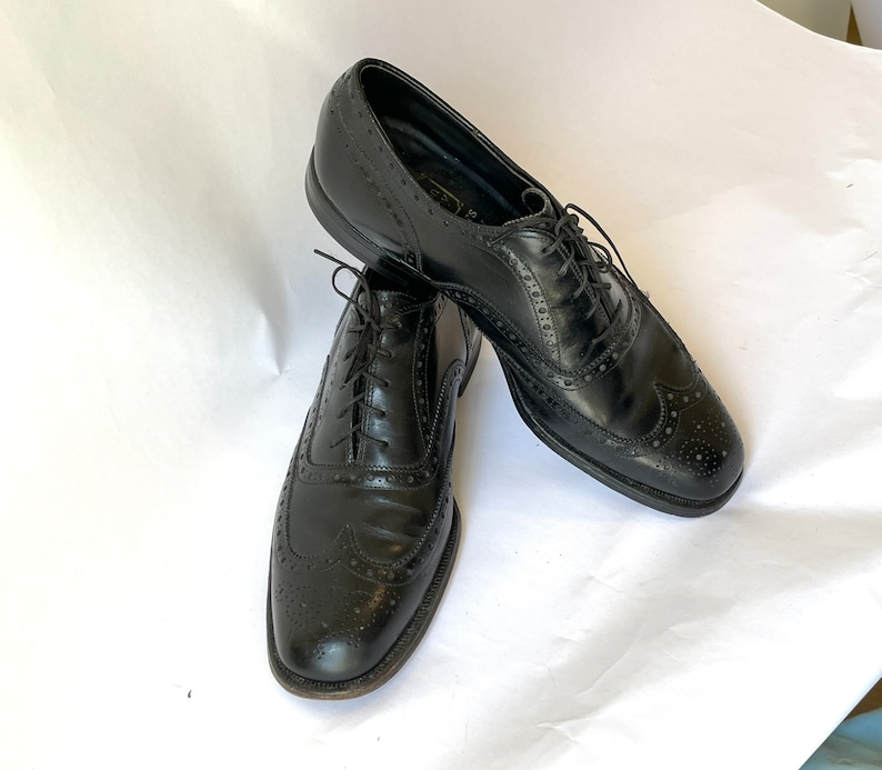 Puede incluir: Un par de zapatos Oxford de cuero negro con detalles de punta de ala. Los zapatos tienen cordones y est&aacute;n en buen estado.