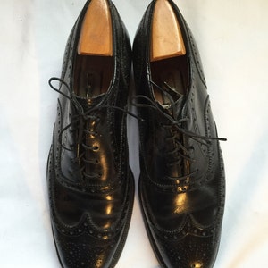 Puede incluir: Un par de zapatos negros de cuero con cordones, punta de ala y patr&oacute;n de brogue.