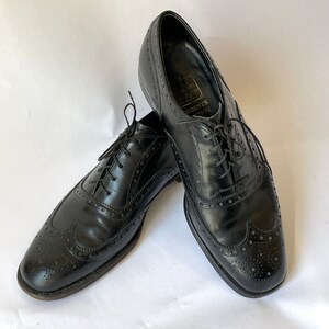 Puede incluir: Un par de zapatos negros de cuero con cordones y detalles de punta de ala. Los zapatos tienen un patr&oacute;n de brogue y est&aacute;n hechos por Johnston & Murphy.