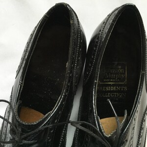 Puede incluir: Un par de zapatos negros de cuero con cordones y detalles de punta de ala. Los zapatos est&aacute;n etiquetados con "Johnson & Murphy" y "Presidents Collection" en el interior.
