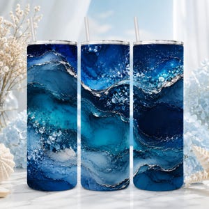 May include: Three cylindrical tumblers featuring a vibrant blue and navy alcohol ink pattern with swirling white and silver metallic accents. Each tumbler has a straight wall design, a clear lid, and a thin, straight straw extending from the top.