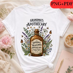 May include: A white t-shirt featuring a graphic of a brown apothecary bottle surrounded by wildflowers, lavender, and butterflies. The text reads: Grandma's Wildflower Apothecary, Botanical Remedies & Herbal Cures, Est. 1954. The design is centred on the chest.