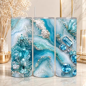 May include: Three cylindrical tumblers with straws, each featuring a vibrant teal and white marbled pattern accented with silver glitter. The design includes detailed illustrations of faceted blue gemstones and crystalline clusters across the surface.