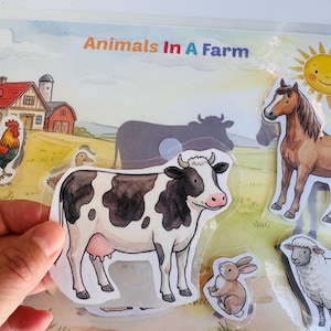 Interactive farm animal activity page showing a child's hand holding a cow cutout ready to be matched on the laminated barnyard scene.