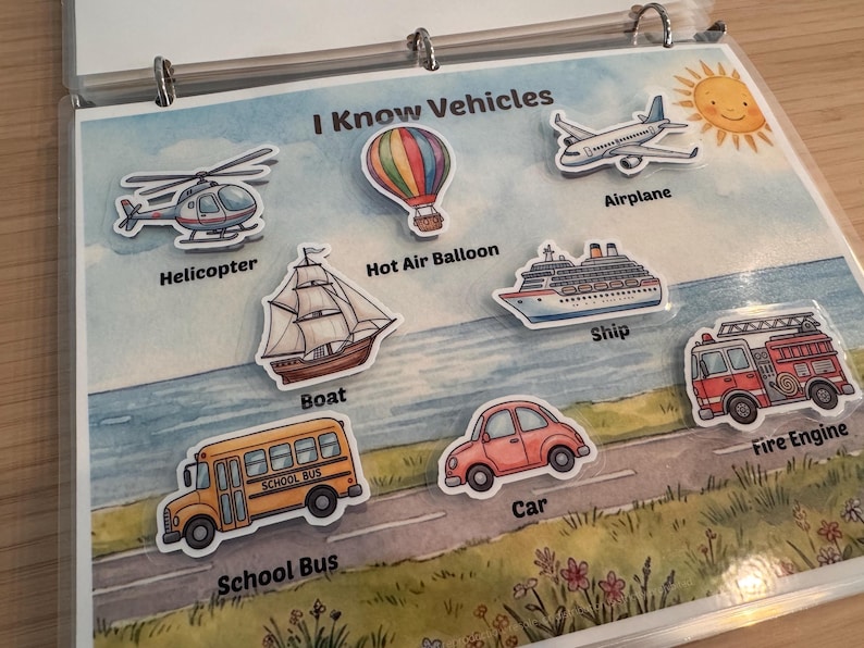 May include: A laminated educational page titled I Know Vehicles featuring watercolor illustrations of a helicopter, hot air balloon, airplane, boat, ship, fire engine, school bus, and car, each labeled with its corresponding name in black text.
