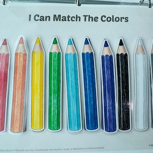 May include: A laminated educational activity sheet titled I Can Match The Colors featuring ten illustrated colored pencils in a row. The pencils are red, orange, yellow, green, light blue, dark blue, dark purple, black, white, and gray.