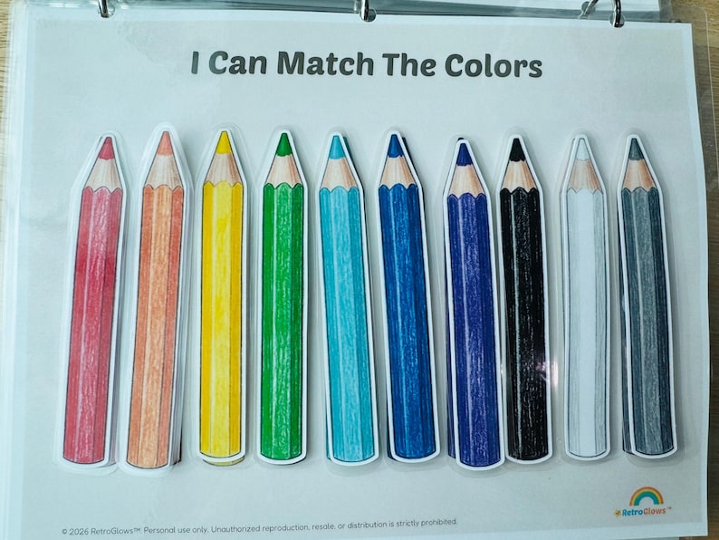 May include: A laminated educational activity sheet titled I Can Match The Colors featuring ten illustrated colored pencils in a row. The pencils are red, orange, yellow, green, light blue, dark blue, dark purple, black, white, and gray.