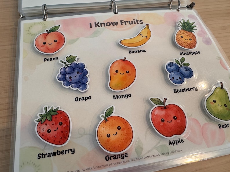 May include: A laminated educational sheet titled I Know Fruits featuring colorful cartoon stickers of a peach, banana, pineapple, grape, mango, blueberry, strawberry, orange, apple, and pear, each labeled with its corresponding name in black text.