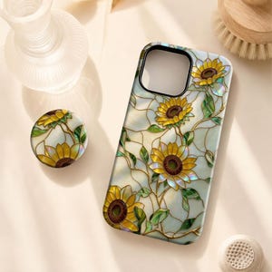 May include: A rectangular phone case and a circular phone grip featuring a stained glass design with yellow sunflowers, green leaves, and dark brown centers against a pearlescent white background with gold-colored outlines throughout the pattern.
