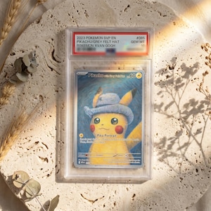 May include: A graded 2023 Pokemon SVP EN Pikachu with Grey Felt Hat trading card, #085, encapsulated in a clear plastic slab. The card features a yellow Pikachu wearing a blue hat against a blue swirling background with the text Pika-Portrait.