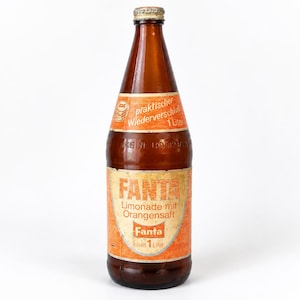 May include: A vintage brown glass bottle with a metal cap, featuring an orange label with the text Fanta Limonade mit Orangensaft and Inhalt 1 Liter. The upper label section includes the text praktischer Wiederverschluss 1 Liter.