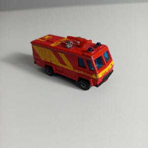 May include: A red die-cast toy fire truck with yellow accents and the text FOAM UNIT 3 and METRO AIRPORT printed on the side. The vehicle features blue tinted windows, black wheels, and a red nozzle mounted on the roof of the cabin.