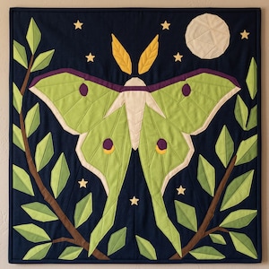 May include: A square fabric wall hanging featuring a large lime green luna moth centered on a dark navy blue background. The moth is surrounded by brown branches with light and dark green leaves, a cream-colored moon, and small yellow stars.