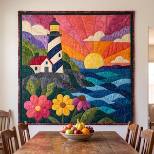 May include: A square fabric wall hanging featuring a pieced quilt design of a lighthouse on a rocky cliff, a sunset with radiating orange and purple rays, a yellow sun, and blue ocean waves. Large pink, yellow, and purple flowers are in the foreground.