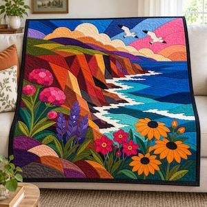 May include: A rectangular quilt featuring a vibrant landscape scene with geometric cliffs, a blue ocean with white waves, and a sky with two flying seagulls. The foreground displays colorful flowers including pink, purple, and orange blossoms.