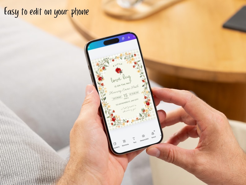 May include: A smartphone displaying a digital invitation template with the text 'A little love bug is on the way' surrounded by a floral border of red roses and yellow flowers. The screen includes editing icons and the text 'Easy to edit on your phone'.