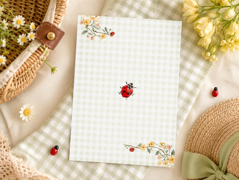 May include: A rectangular stationery sheet featuring a light green and white gingham pattern. The design includes a small red ladybug in the center and floral illustrations with yellow and orange blossoms in the top left and bottom right corners.