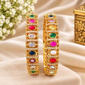 Pode incluir: Dois braceletes dourados com um design de treliça incrustado com pequenos cristais transparentes. Cada bracelete apresenta uma fila vertical de pedras preciosas ovais multicoloridas, incluindo tons vermelhos, rosas, verdes, azuis e brancos em um padrão.