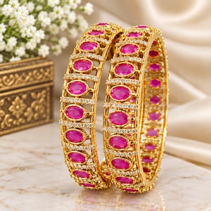 Peut inclure: Deux bracelets rigides dorés ornés d'une série de pierres ovales rose vif disposées verticalement. Chaque bracelet est agrémenté de rangées de petites pierres claires et scintillantes bordant le cadre métallique, créant un design structuré.