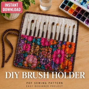 May include: A fabric brush holder featuring a vibrant floral pattern with pink, orange, and purple flowers on a dark background. The holder has multiple vertical slots containing various paintbrushes and includes long fabric ties for securing it.