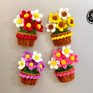 May include: Four pipe cleaner flower arrangements in brown pots. The top left has red and white flowers with yellow centers. The top right has yellow and white flowers with brown centers. The bottom left has purple and white flowers. The bottom right has pink and white flowers.
