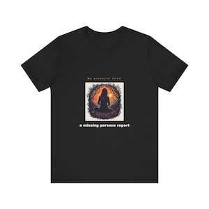 Op de afbeelding: Een zwart t-shirt met korte mouwen en een centrale afbeelding van een silhouet dat in een bos zit bij zonsondergang. Boven de afbeelding staat de tekst "My potential filed" en onder de afbeelding de tekst "a missing persons report" in het wit.