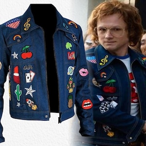 May include: A dark blue denim jacket featuring a variety of colourful embroidered patches including a cherry, a rocket, a cactus, lips, a pineapple, a rainbow, a treble clef, playing cards, and an American flag, with a pointed collar and front zip.