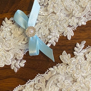 May include: White lace garter with a light blue satin bow and a rhinestone embellishment.